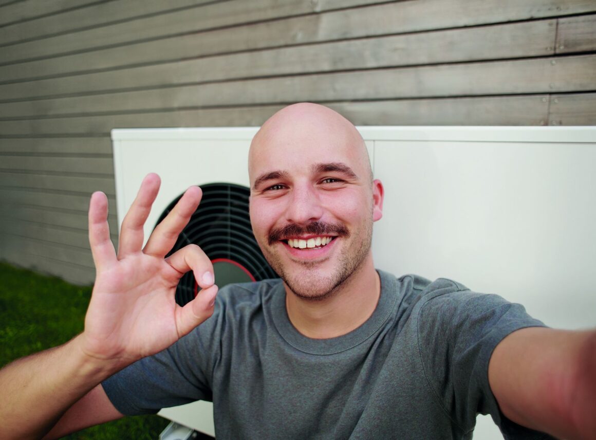 Uśmiechnięty mężczyzna na tle pompy ciepła GeniaAir Split marki Saunier Duval