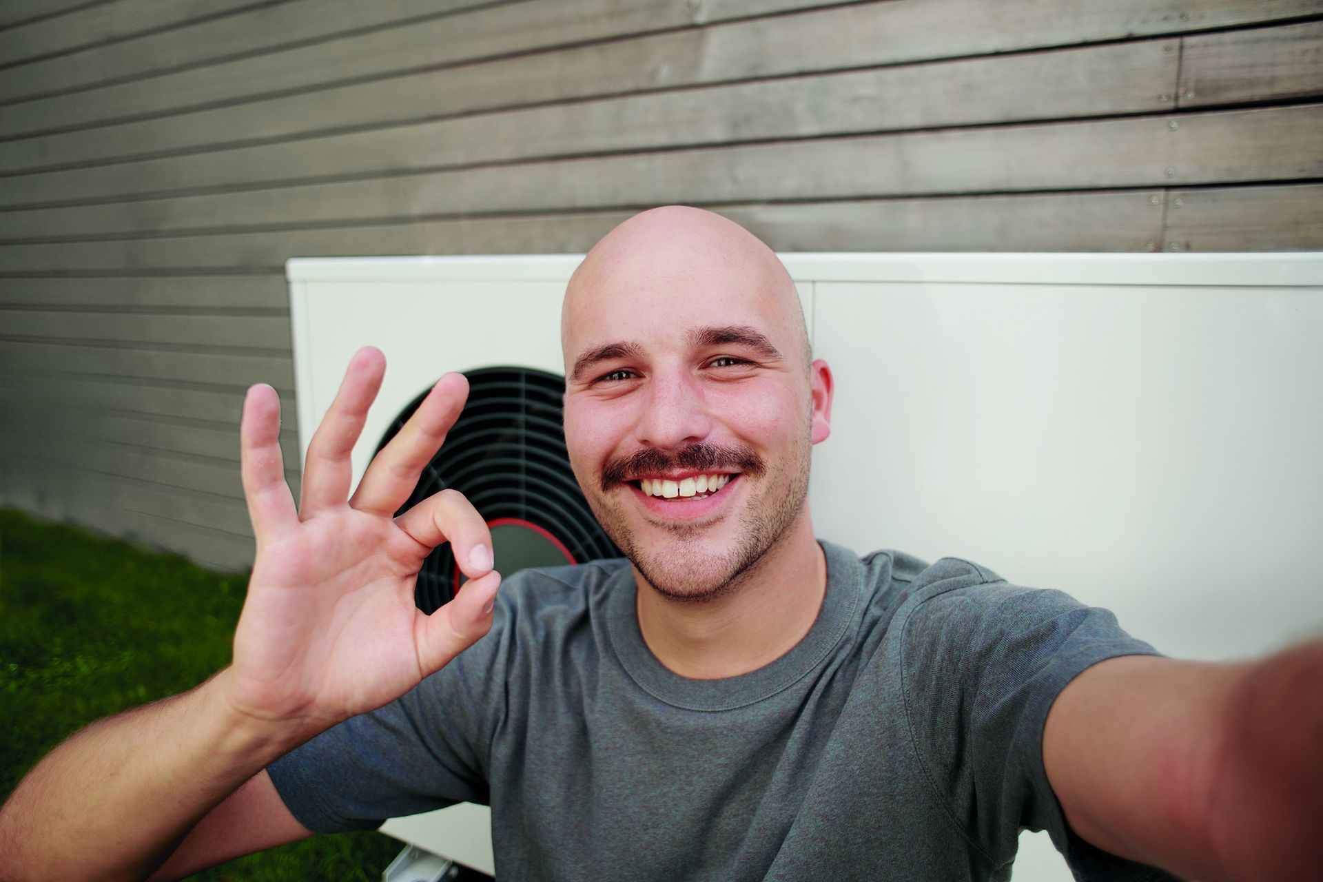 Uśmiechnięty mężczyzna na tle pompy ciepła GeniaAir Split marki Saunier Duval